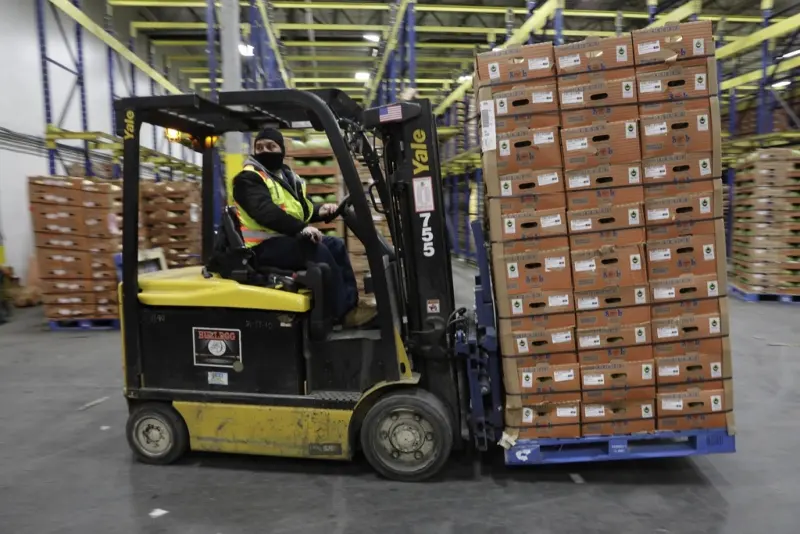 Forklift operator moving a loaded pallet in a warehouse