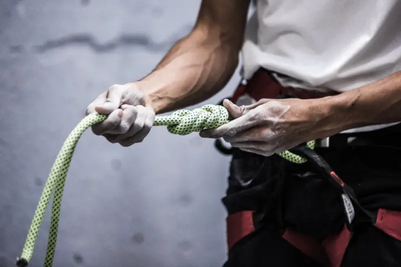 Hands gripping a rope attached to a harness